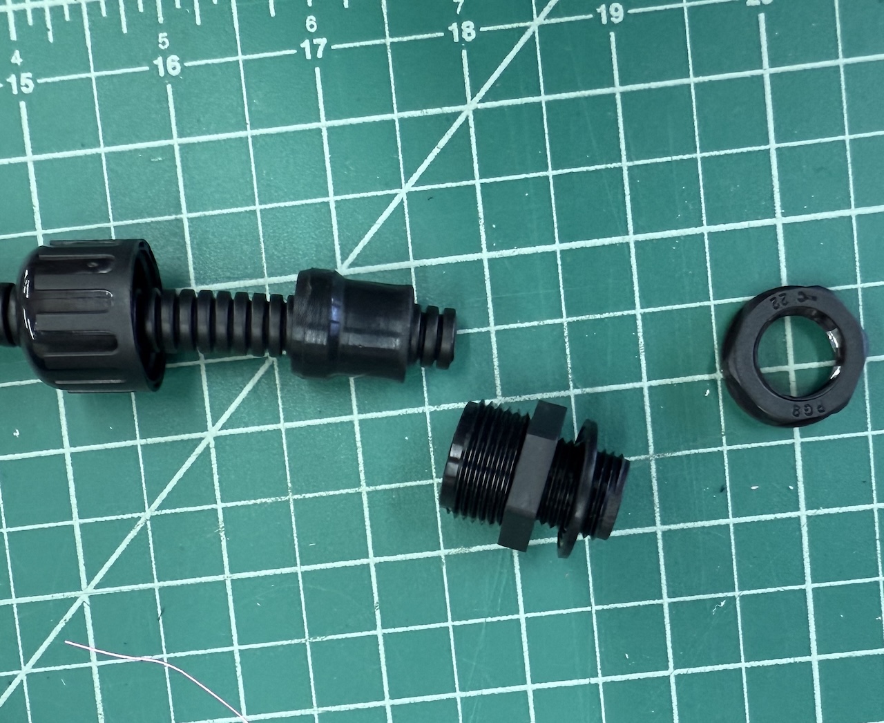 Disassembled ethernet conduit assembly, showing the plastic nut, body, glad and conduit, with a flexible bushing on a green self healing cutting mat.